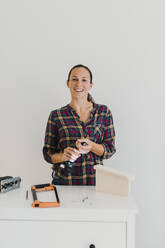 Smiling woman changing drill bit while standing at home - DMGF00400