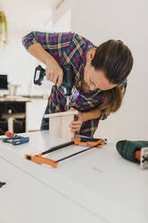 Woman doing fitting screw with electric screwdriver while working at home - DMGF00413