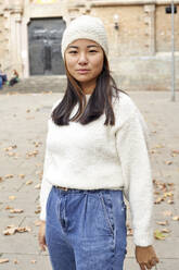 Young woman wearing knit hat standing on street in city - VEGF03242