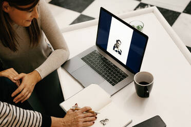 Daughter looking at black and white photo on laptop while sitting by mother at home - ERRF04766