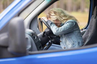 Woman with blond hair resting on steering wheel in van - WPEF03759