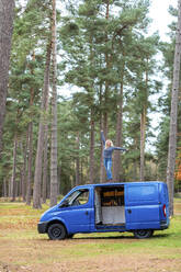 Sorglose Frau mit erhobenen Armen auf dem Dach eines Wohnmobils in Cannock Chase - WPEF03769