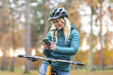 Glückliche Frau mit blondem Haar, die in Cannock Chase ein Mobiltelefon benutzt - WPEF03797