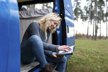 Happy woman reading book on door of camper van at Cannock Chase - WPEF03820