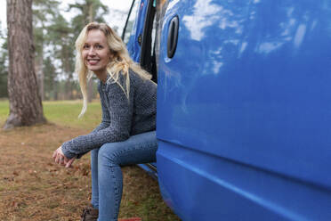 Smiling woman sitting on door of camper van at Cannock Chase - WPEF03821
