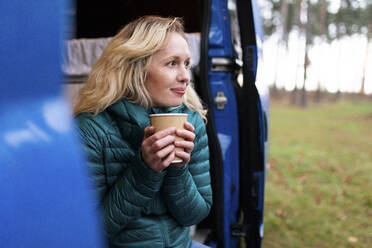 Thoughtful woman with disposable tea cup looking away at door of motor home - WPEF03823