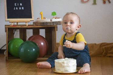 Niedlicher kleiner Junge isst Kuchen, während er zu Hause auf dem Boden sitzt - NGF00724