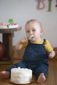 Kleiner Junge isst Kuchen an seinem ersten Geburtstag, während er zu Hause sitzt - NGF00725