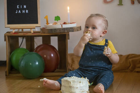 Baby boy eating his first birthday cake while sitting on floor at home - NGF00727