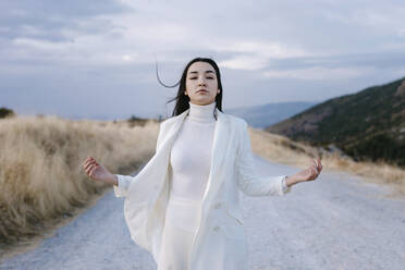 Young woman wearing white jacket standing on road - TCEF01409