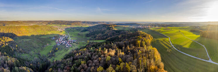 Drohnenansicht eines Dorfes umgeben von einem Herbstwald bei Sonnenaufgang - STSF02697