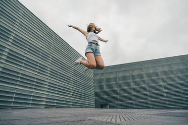 Carefree woman with arms outstretched jumping against wall - MTBF00730