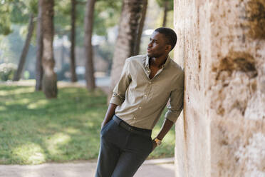 Thoughtful businessman leaning on wall in park - EGAF01194