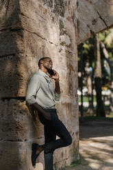 Male entrepreneur talking on smart phone with hand in pocket at park - EGAF01199