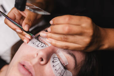 From above of crop anonymous master doing eyelash extension after mapping for unrecognizable female customer in face mask - ADSF18641