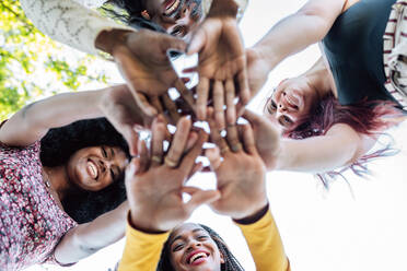 From below of group of multiracial cheerful women standing together and stacking hands in name of unity and friendship - ADSF18688