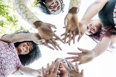 From below of group of multiracial cheerful women standing together and stacking hands in name of unity and friendship - ADSF18689