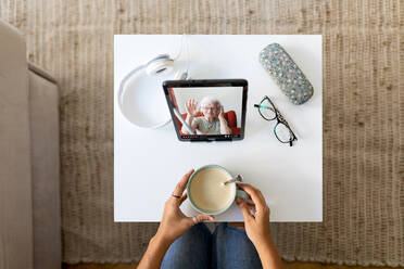 From above of unrecognizable female watching video of tablet while sitting at table with cup of coffee and spending weekend at home - ADSF18756