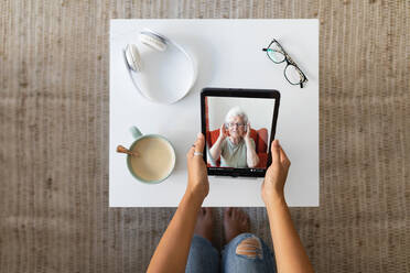 From above of unrecognizable female watching video of tablet while sitting at table with cup of coffee and spending weekend at home - ADSF18757