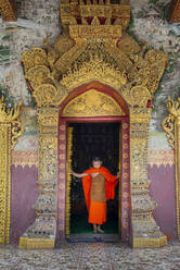 Ein junger buddhistischer Mönch an den Türen eines buddhistischen Tempels, Luang Prabang, Laos, Indochina, Südostasien, Asien - RHPLF18488