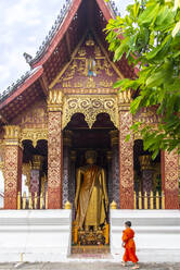 Ein junger buddhistischer Mönch steht vor einer großen Statue des Goldenen Buddha in Luang Prabang, Laos, Indochina, Südostasien, Asien - RHPLF18494