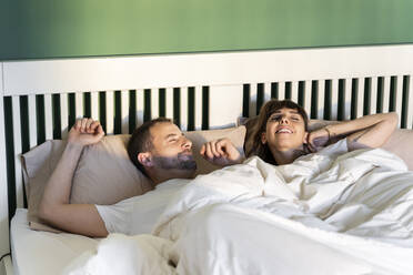 Smiling couple waking up slowly while lying on bed at home - AFVF07705