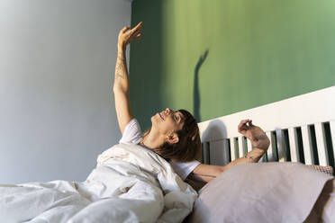 Smiling woman stretching while sitting on bed at home - AFVF07709