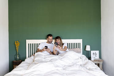Glückliche Frau, die einem Mann, der zu Hause auf dem Bett sitzt, ihr Mobiltelefon zeigt - AFVF07717