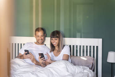 Mittleres erwachsenes Paar lächelt bei der Benutzung eines Mobiltelefons zu Hause - AFVF07718