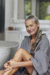 Mature woman sitting near bathtub in bathroom - MCF01508