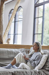 Thoughtful mature woman looking away while holding coffee cup at home - MCF01514