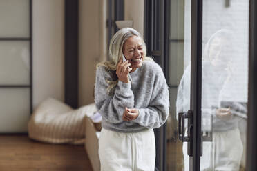 Laughing mature woman with eyes closed talking on phone at home