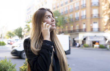Young woman talking on mobile phone while standing on street in city - JCCMF00091
