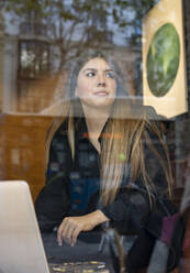 Woman with laptop looking away while sitting at cafe - JCCMF00097