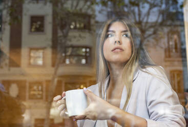 Junge schöne Frau hält Kaffeetasse, während sie im Café sitzt - JCCMF00104