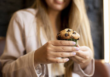 Woman holding chocolate chip muffin while sitting at cafe - JCCMF00105