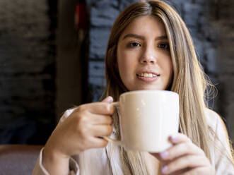 Young woman drinking coffee while sitting in cafe - JCCMF00107