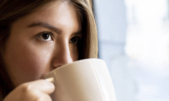 Nahaufnahme einer Frau, die beim Kaffeetrinken im Café wegschaut - JCCMF00110