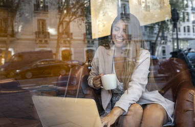 Lächelnde Frau, die einen Laptop benutzt, während sie in einem Café Kaffee trinkt - JCCMF00111