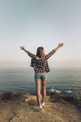 Young woman with arms outstretched standing against clear sky - MTBF00745