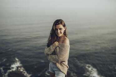 Lächelnde Frau, die wegschaut, während sie am Meer steht - MTBF00747