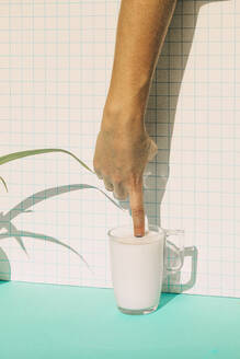 Female putting finger in milk cup on blue table - ERRF04792