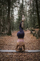 Young athlete headstand with legs crossed at knee in forest at Ordesa National Park, Huesca, Spain - ACPF00962