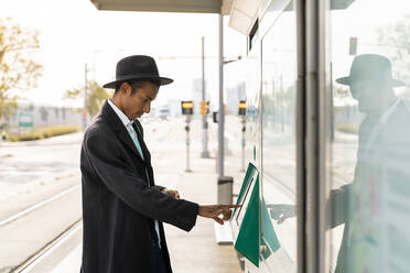 Young man using ticket machine at tram stop - AFVF07725