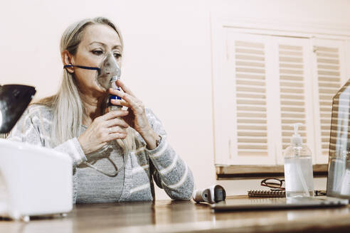 Senior woman using nebulizer during online consultation doctor at home - ERRF04810