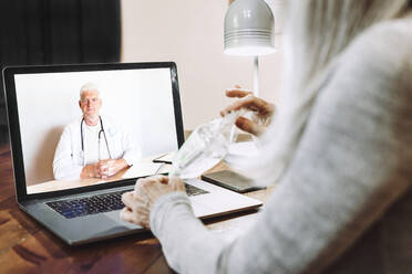 Senior woman showing medical sample to doctor on video call at home - ERRF04829