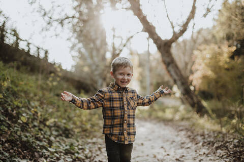 Carefree boy standing with arms outstretched in forest stock photo