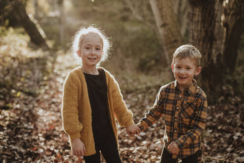 Bruder und Schwester lächelnd und händchenhaltend im Wald stehend - GMLF00886
