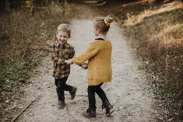 Smiling girl and brother holding hands while playing in forest - GMLF00890