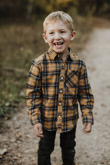 Lächelnder Junge mit kariertem Hemd auf einem Fußweg im Wald - GMLF00891